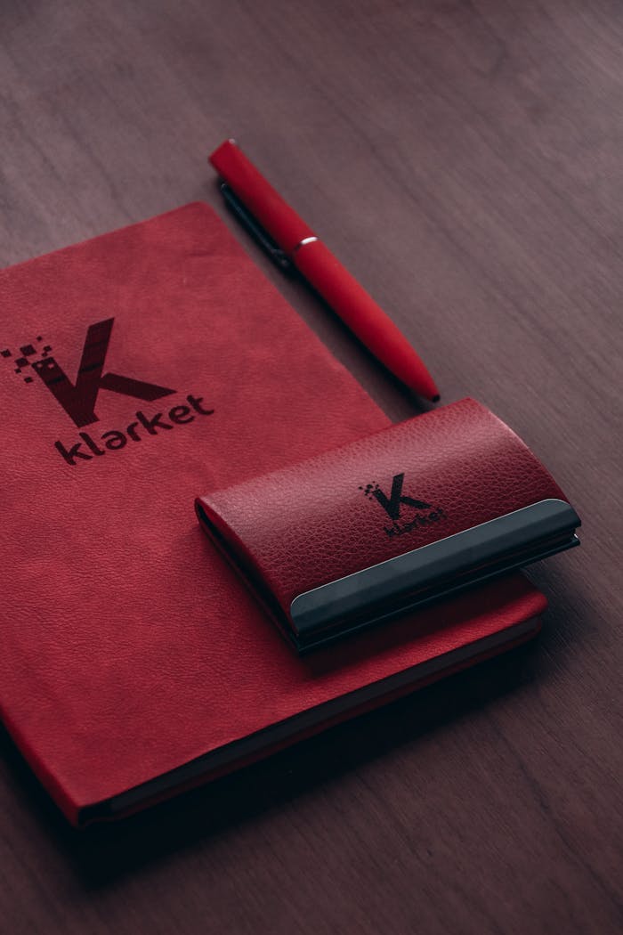 Red notebook with branding and pen on wooden desk, ideal for office themes.